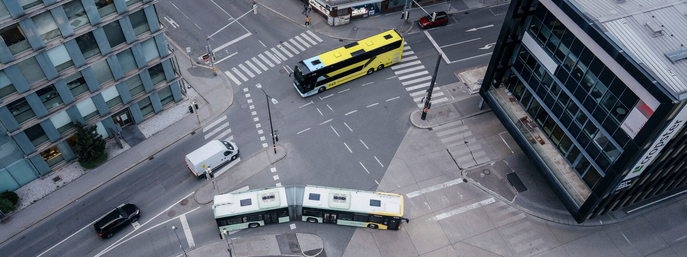Das Foto ist in der Vogelperspektive aufgenommen und zeigt eine Straßenkreuzung am Innsbrucker Bahnhof. Zu sehen sind neben drei anderen Autos auch zwei VVT Busse im Straßenverkehr.