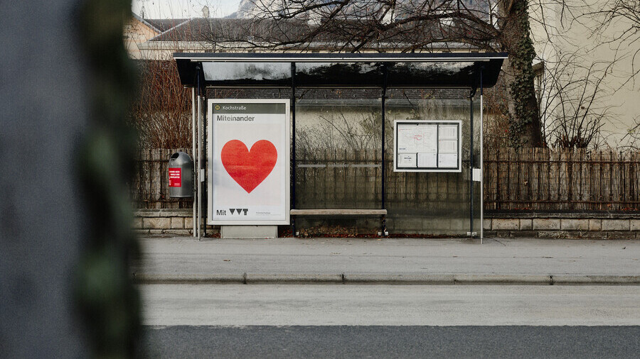 Am Bild zu sehen ist eine Bushaltestelle mit den Plakat der Miteinander Kampagne. Es ist wei&szlig; und in der Mitte ist ein gro&szlig;es rotes Herz. Dar&uuml;ber steht 'Miteinander', darunter 'mit VVT'.